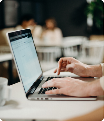 Person using a laptop with a blurred background of people and decor