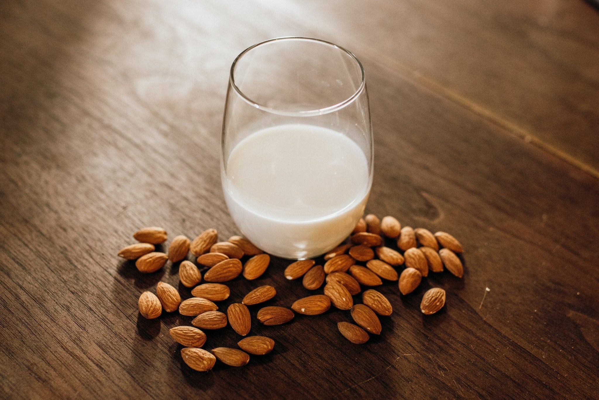 glass of almond milk surrounded by almonds