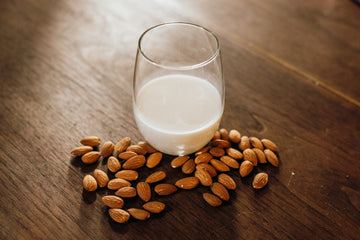 glass of almond milk surrounded by almonds