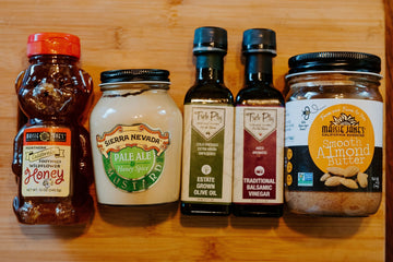honey, mustard, vinaigrette and Almond butter jars lined up on cutting board