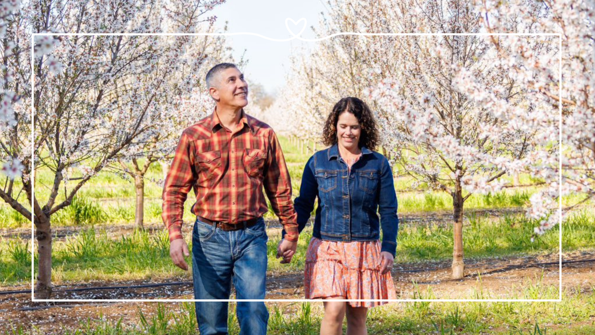 Maisie and Isidro walking in an almond orchard in bloom