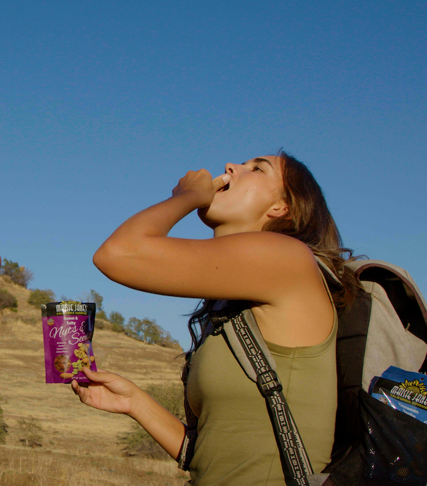 Woman hiking and stoping to eat out of her Maisie Jane's snack packs