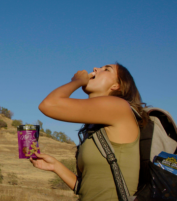 Woman hiking and stoping to eat out of her Maisie Jane's snack packs