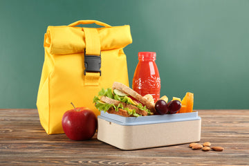 yellow lunchpail with a container of food next to it along with a red juice and apple