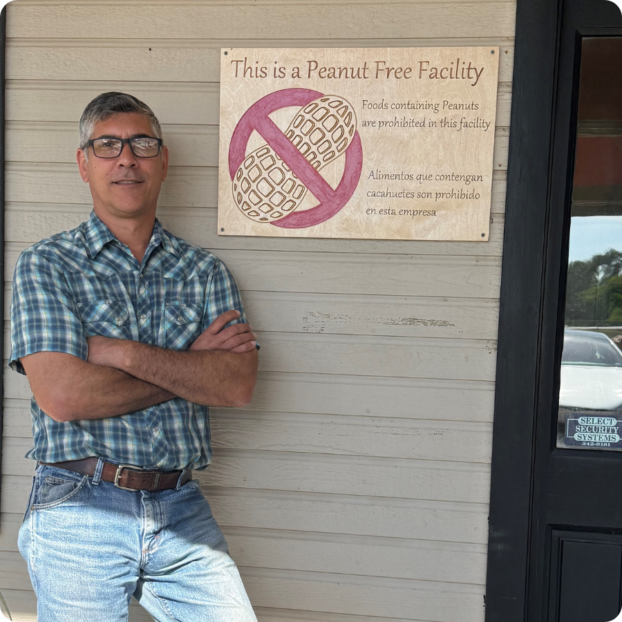 Man standing in front of a 'Peanut Free Facility' sign on a wooden door.