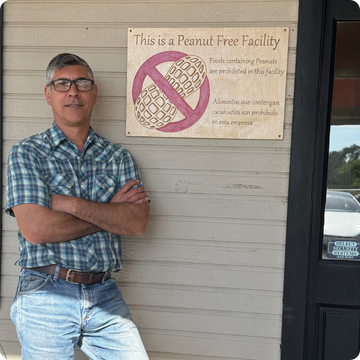 Man standing in front of a 'Peanut Free Facility' sign on a wooden door.