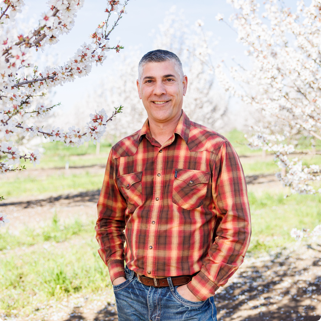 Isidro in a plaid shirt standing in an orchard with blooming trees