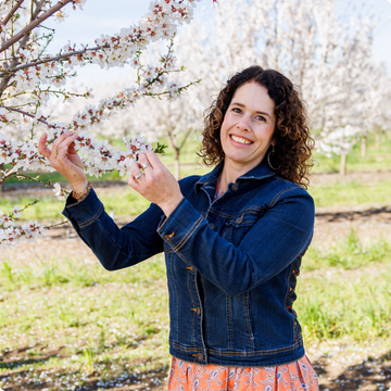 Maisie in a blue jacket standing in a almond blossom orchard
