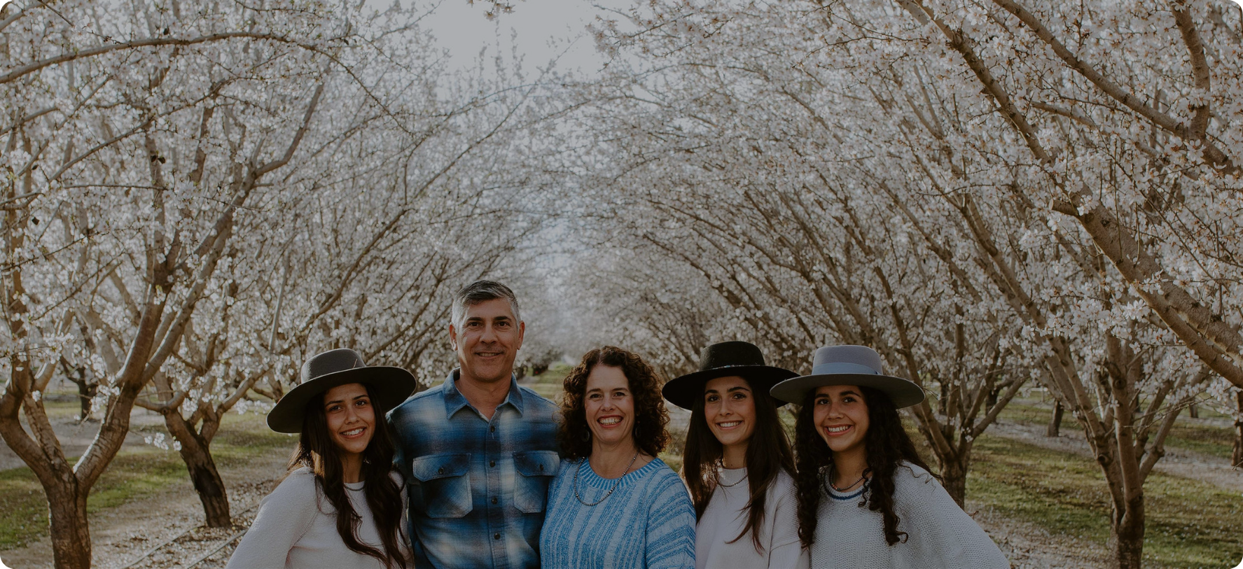 Maisie Jane's family of five posing in an almond blossom orchard